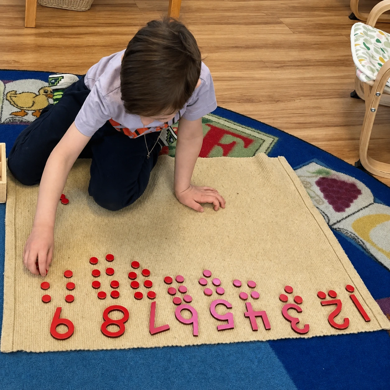 A Montessori Casa child arranging number counters on a classroom mat.
